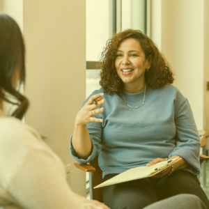 Woman sitting with legs crossed holding a clipboard and talking to someone as part of a job performance review