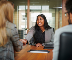First day at a new job person sitting at a desk, smiling and shaking new employers hand for their first day at a new job