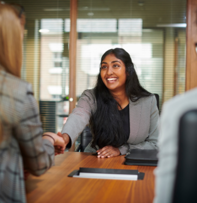 First day at a new job person sitting at a desk, smiling and shaking new employers hand for their first day at a new job